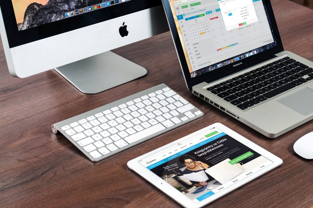 Macbook, lapotop, and tablet on desk displaying graphics and other infomation. 