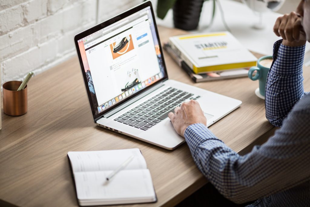 A business man sat at a desk pondering shared hosting over his laptop with an open notebook beside him. 