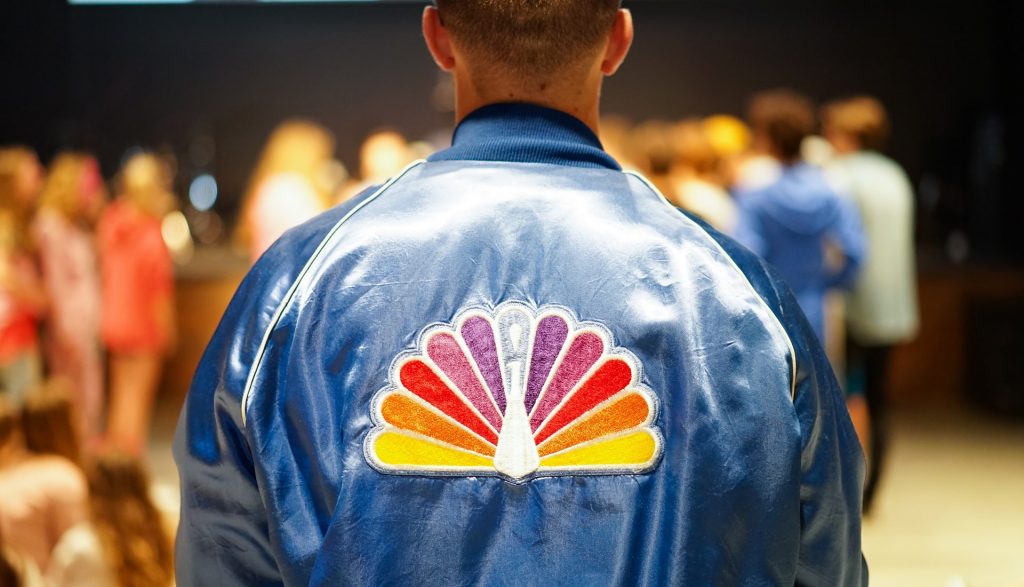 A person wearing a jacket with the NBC Peacock logo printed on it.